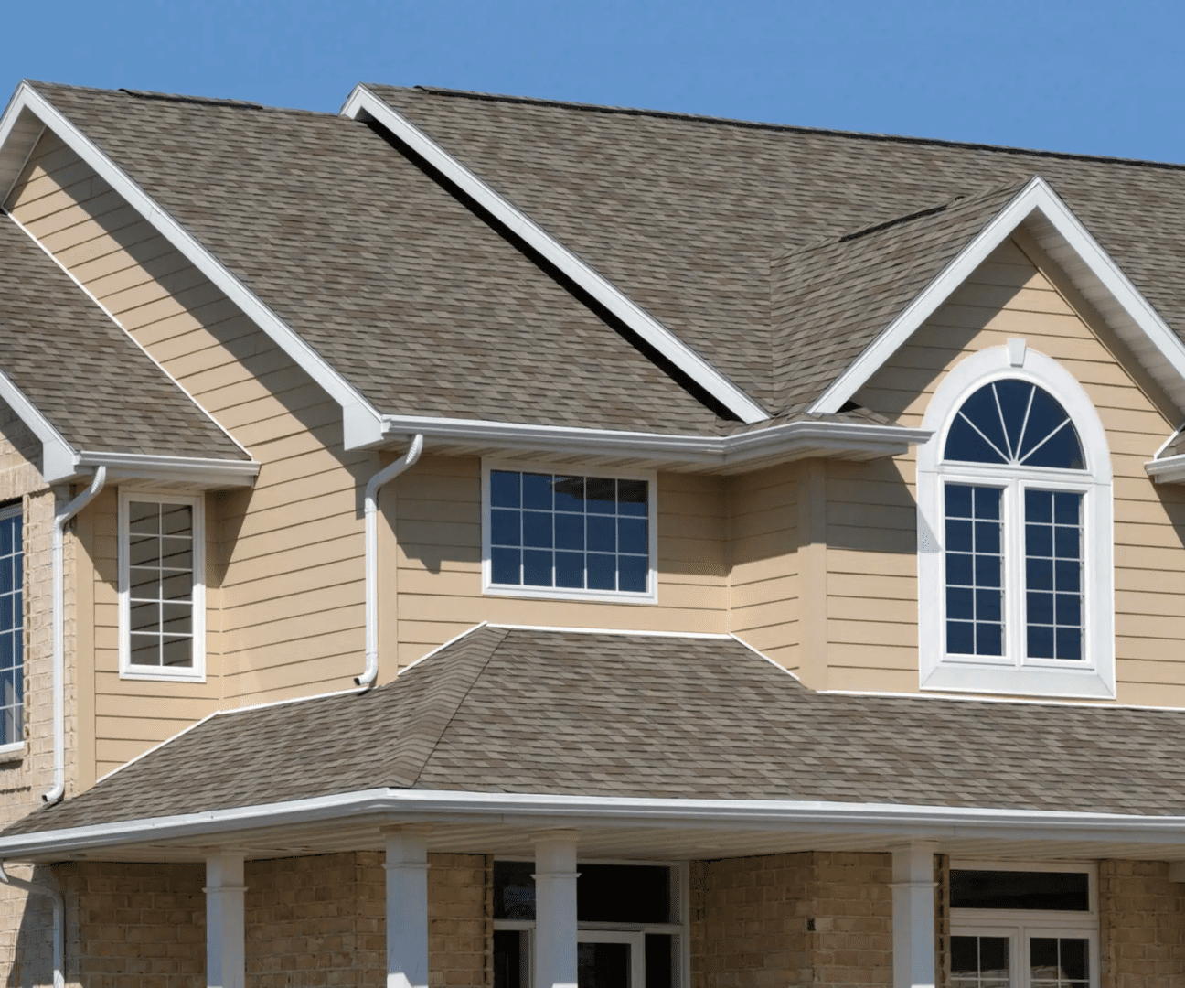A modern beige house with multiple peaked roofs and large windows under a clear blue sky.