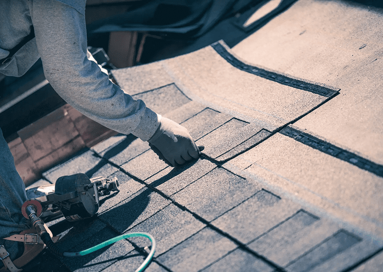 A person installing asphalt shingles on a roof.